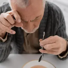 Starszy mężczyzna z drżącą ręką próbuje jeść. Choroba parkinson ile się żyje, to pytanie, które zadaje sobie wielu.