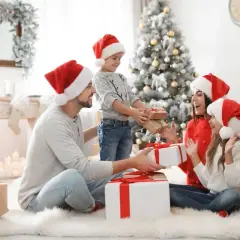 Rodzina w czapkach Mikołaja wymienia się prezentami przy choince.