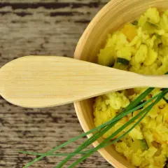 Risotto allo zafferano cremoso con zucchine e peperoni, guarnito con erba cipollina e un cucchiaio di legno.