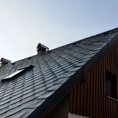 Dach pokryty ciemnym łupkiem, z widocznymi okienkami dachowymi i kominami. Drewniana ściana domu dodaje mu rustykalnego charakteru.