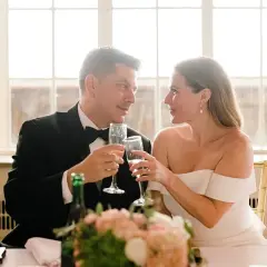 Para młoda wznosi toast kieliszkami szampana. W tle okna, idealne na romantyczne piosenki na wesele.