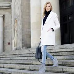 Elegancka kobieta w białym płaszczu i jeansach schodzi po schodach. Stylowe biały płaszcz stylizacje na co dzień.