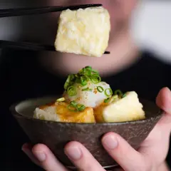 Chopsticks lift a piece of crispy age tofu, ready to be dipped into a savory sauce.