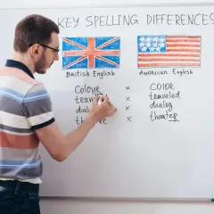 Profesor explica las diferencias de ortografía entre los tipos de inglés: británico y americano, con ejemplos escritos en la pizarra.