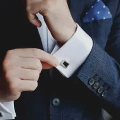 Mann schließt Manschettenknöpfe an seinem Hemd. Was ist eine Manschette? Ein elegantes Accessoire, das den Hemdsärmel verschließt und Stil verleiht.