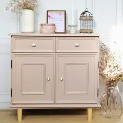Un meuble en bois, fraîchement peint en rose poudré, est décoré de fleurs séchées et d'une cage à oiseaux.