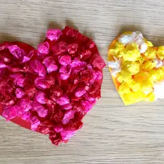 Zwei bunte Herzen, rot und gelb, mit zerknülltem Seidenpapier beklebt. Ein schönes Beispiel für herz basteln kinder.
