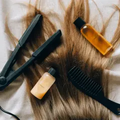 Plancha, peine y botellitas de champú y acondicionador sobre cabello rubio. Una solución casera para el pelo naranja.