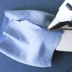 Ironing a folded cuff band to a light blue sleeve. This step is crucial for how to sew a folded cuff band to a sleeve.
