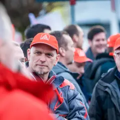 Männer in roten Kappen mit IG Metall Logo, diskutieren über die leistungszulage.