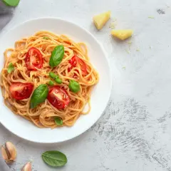 Leckere Tagliatelle Rezepte: Spaghetti mit Tomaten, Basilikum und Parmesan auf einem Teller, daneben goldene Gabel und Messer.