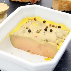 Un foie gras mi-cuit, à la texture parfaite, est servi dans un plat blanc, parsemé de grains de poivre. La température idéale pour savourer ce délice.
