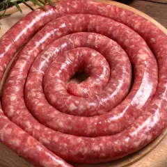 Surowa, zwinięta w spiralę salsiccia na drewnianej desce, ozdobiona gałązkami rozmarynu.