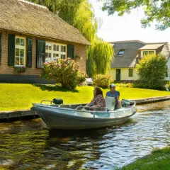 Ein Paar genießt eine Bootsfahrt durch das malerische Klein Venedig Holland, vorbei an reetgedeckten Häusern und üppigem Grün.