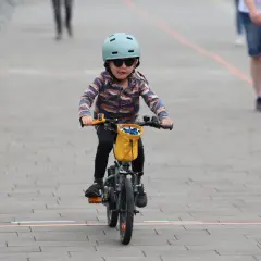 Małe dziecko w kasku i okularach przeciwsłonecznych śmiga na rowerze, wyciągając język. To dziecko na rowerze przepisy, jak prawdziwy mistrz.