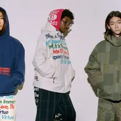 Trzech mężczyzn w ubraniach z kolekcji Junya Watanabe x Supreme. Jeden w granatowej bluzie, drugi w białej kurtce z tekstem, trzeci w zielonej, patchworkowej kurtce.