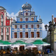 Kolorowe kamienice na szczecińskim Starym Mieście, z kawiarnianymi ogródkami i latarnią.