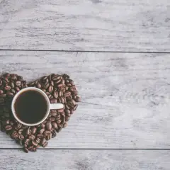 Una tazzina di caffè nero, circondata da chicchi di caffè disposti a forma di cuore su un tavolo di legno. Un invito al caffè in allattamento.