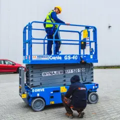 Dwóch pracowników w kaskach i kamizelkach na podnośniku koszowym Genie GS-40.