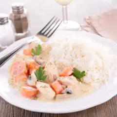 Une assiette de blanquette de veau crémeuse avec des carottes et des champignons, servie avec du riz blanc. Un verre de vin de Bordeaux est suggéré pour accompagner ce plat.
