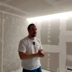 Mężczyzna prezentuje sufit podwieszany z wnęką na led, w trakcie prac wykończeniowych.