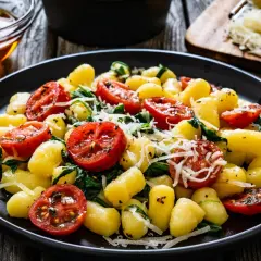 Pyszne gnocchi ze szpinakiem i pomidorkami koktajlowymi, posypane parmezanem. Danie wygląda apetycznie.