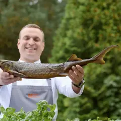 Uśmiechnięty kucharz prezentuje wędzonego jesiotra słodkowodnego.