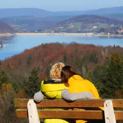 Para idealna na bieszczady na weekend. Dwie osoby siedzą na ławce, przytulając się, patrząc na jezioro i jesienne wzgórza.