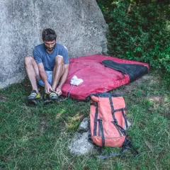 Man förbereder sig för kjugekull bouldering, spänner sina skor bredvid en tjock madrass och en orange ryggsäck.