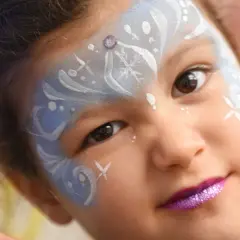 Bambina con trucco da fata del ghiaccio per il carnevale, con glitter viola sulle labbra e disegni bianchi e azzurri sul viso.