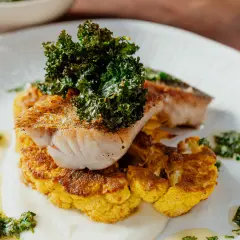Poisson grillé sur un lit de chou-fleur plancha, garni de kale croustillant et d'une sauce verte.