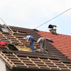 Deux couvreurs travaillent sur une toiture en cours de rénovation, préparant à prolonger un toit existant.