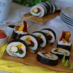 Pyszne sushi z kurczakiem, papryką i mango na desce. Obok miseczka z imbirem i sos sojowy.