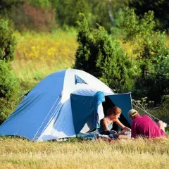 Para spędza czas w namiocie, idealne miejsce na biwak. Otoczeni zielenią i polnymi kwiatami, cieszą się spokojem natury.