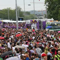 Folla festante a Zurigo per una street parade. Persone danzano e salutano dai carri colorati, un camion speciale trasporta la musica.