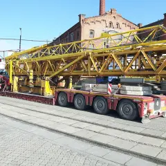 Ciężarówka z przyczepą transportuje żółty element dźwigu. Wymaga to zezwolenia na transport ponadgabarytowy.
