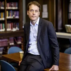 Sven Beckert sitzt in einer Bibliothek, umgeben von Büchern.