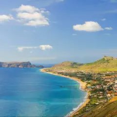 Widok na wybrzeże z plażą, miasteczkiem Vila Baleira i skalistymi wysepkami na oceanie.
