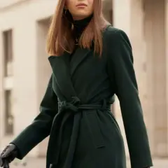 Elegancka kobieta w ciemnozielonym płaszczu z paskiem. Dowiedz się, jak prać płaszcz z wełny i poliestru, by zachował swój kształt.