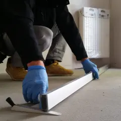 Inspektor w niebieskich rękawiczkach mierzy poziom podłogi poziomicą w nowym mieszkaniu.