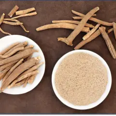 Getrocknete Ashwagandha-Wurzeln und Pulver auf braunem Untergrund. Withaferin A ist ein wichtiger Inhaltsstoff.