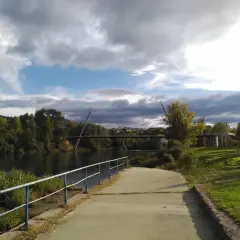 Paseo junto al río Miño, con el puente del Milenio y la playa fluvial de Ourense al fondo. Nubes amenazantes en el cielo.