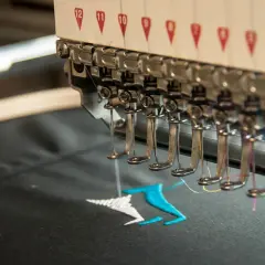 Machine à broder en action, créant un motif coloré sur un tissu noir. La **direct to garment printing** permet des personnalisations uniques.