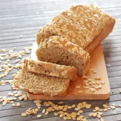 Pane proteico integrale, cosparso di fiocchi d'avena, affettato su un tagliere di legno.