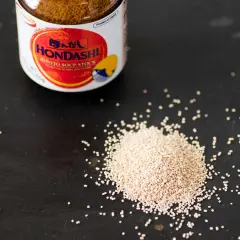 A jar of Hondashi soup stock sits next to a pile of granules. This image helps visualize the dashi powder to water ratio for perfect Japanese broth.