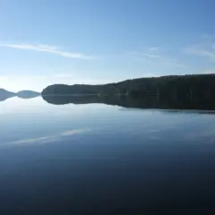 Calmo lago riflette la foresta e il cielo azzurro. Chissà se è il lago più grande d'Europa, con questa pace.