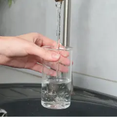 Main tenant une éprouvette graduée sous un robinet, on teste la qualité de l'eau pour s'assurer qu'elle respecte les normes TDS eau potable.