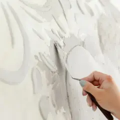 Mano che lavora con uno strumento su uno stucco murale in rilievo, creando un'opera d'arte tridimensionale.
