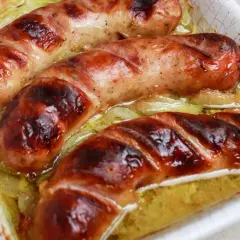 Soczysta, rumiana biała kiełbasa pieczona w piekarniku, skropiona tłuszczem i podana z cebulką.