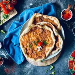 Lahmacun rezept original: Fladenbrot mit Hackfleisch, Tomaten, Petersilie und Käse, daneben Oliven und ein Wrap.